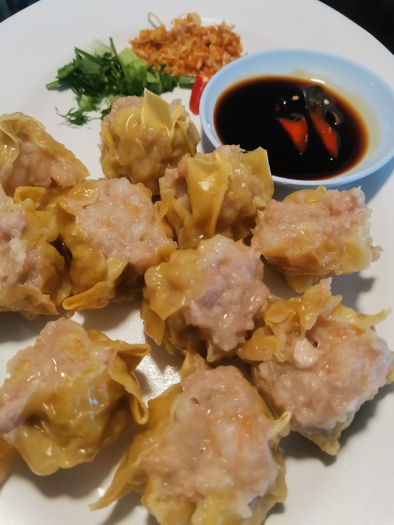 ขนมจีบนึ่งหลายชิ้นในจาน กับถ้วยซีอิ๊วพริกและผักสด